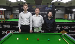 Iulian Boiko and Shachar Ruberg pose for a photo stood either side of the referee and behind the winner's trophy.
