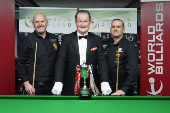 Peter Sheehan and David Causier pose with cues at the table either side of Aonghus McAnally and the trophy.