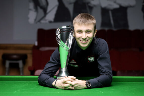 Antoni Kowalski leans on the table with his Q Tour trophy next to his face.