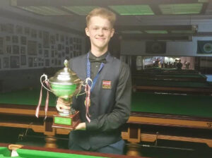 Artemijs Žižins lifts the trophy by the table.