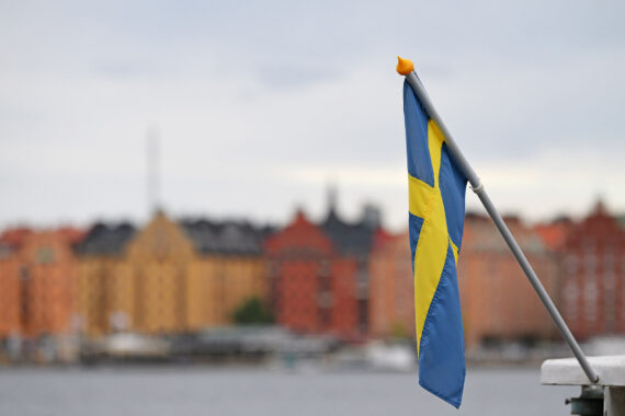 A picture of Stockholm behind the water and with the Swedish flag in the forefront of image.