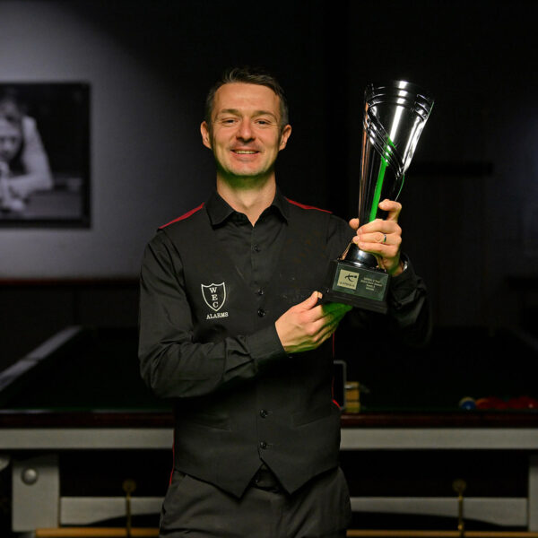 Michael Holt in his waistcoat, shirt and trousers lifts the Q Tour trophy in front of a snooker table.